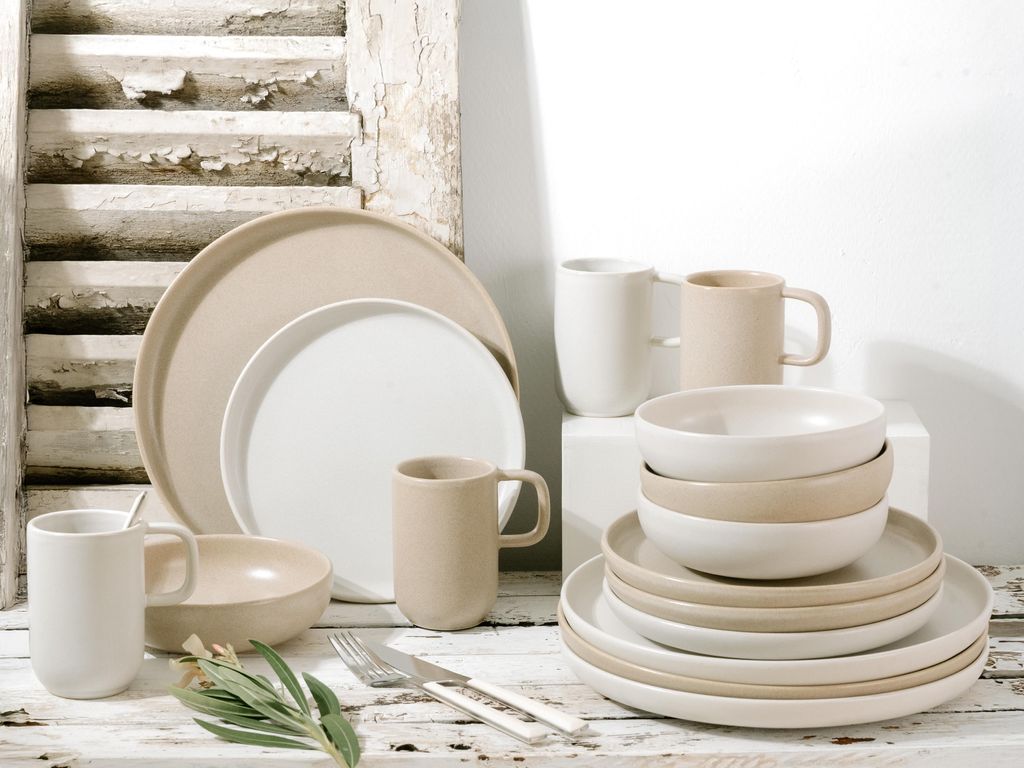 A collection of stoneware plates and mugs arranged on a rustic wooden surface.