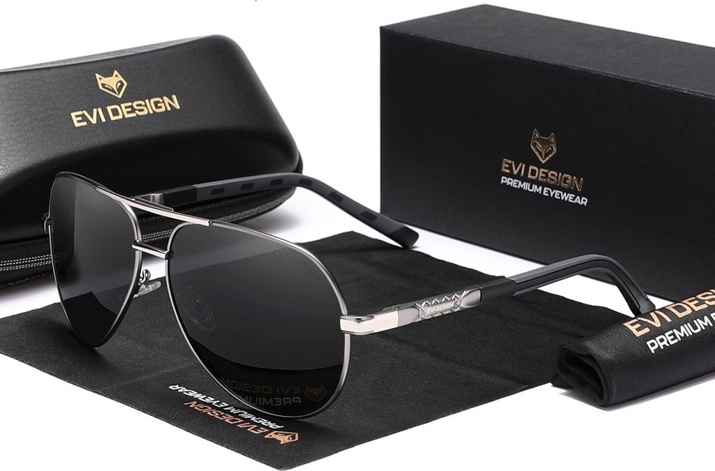 A pair of aviator sunglasses with their case and box are displayed on a black cloth.