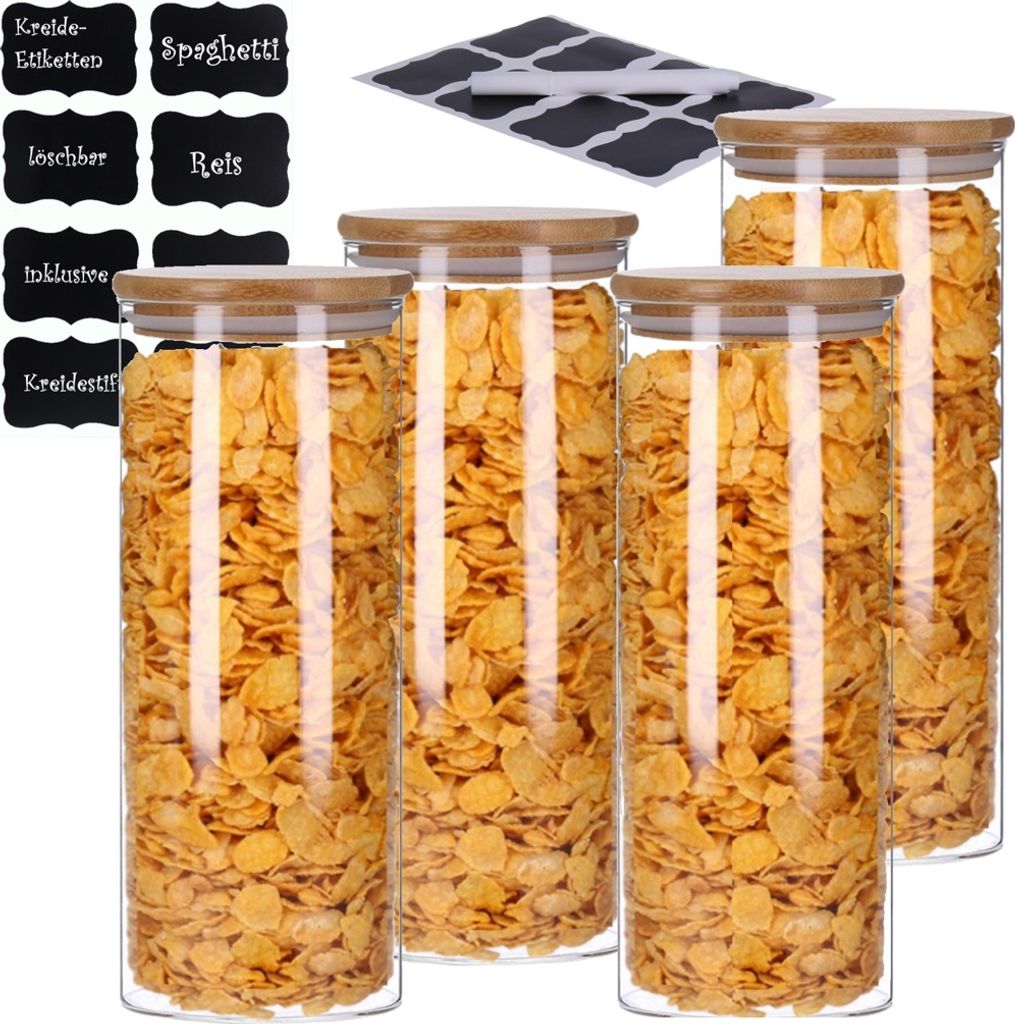 A set of four glass storage jars filled with cereal, with a stack of chalk labels in the background.