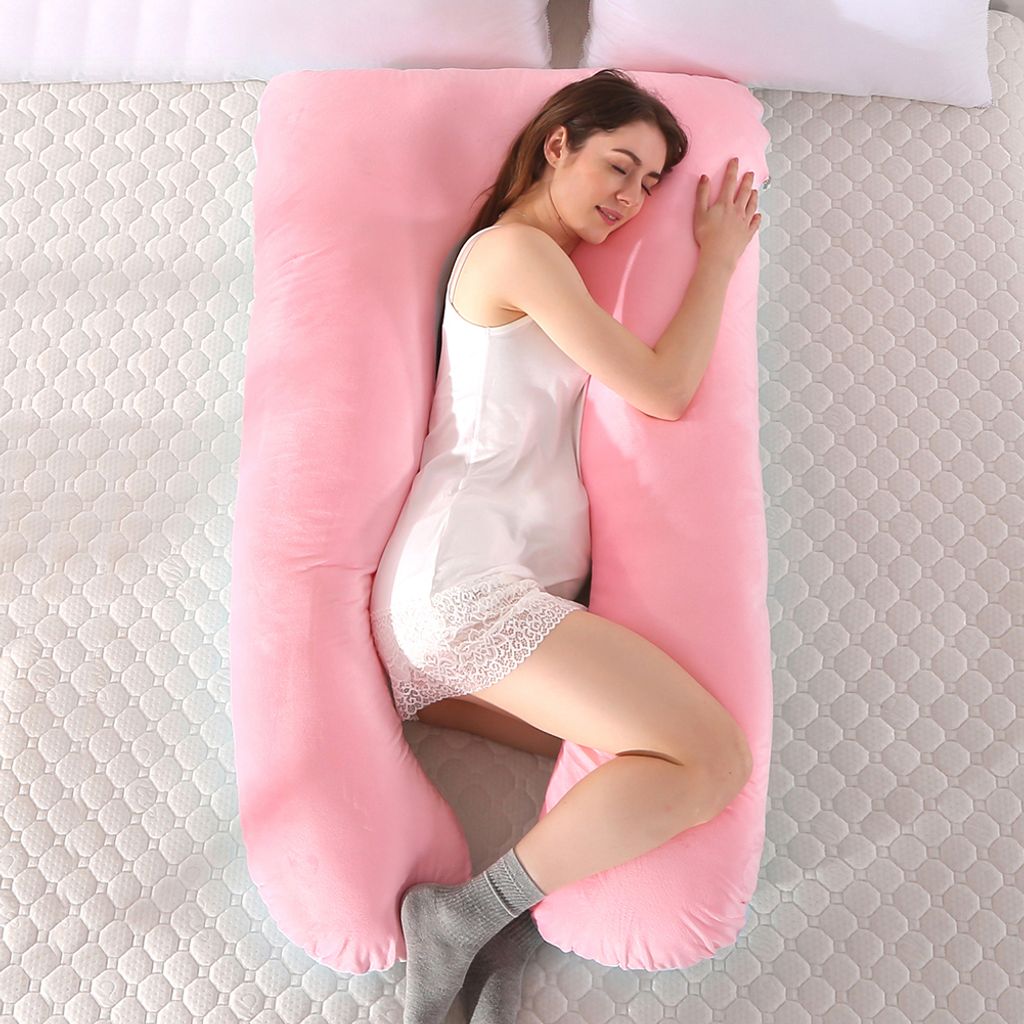A woman is sleeping on a large U-shaped pink pregnancy pillow.