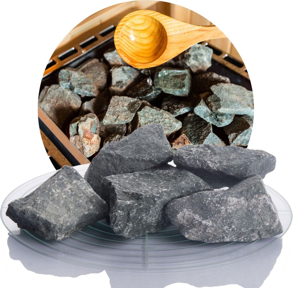A pile of dark gray sauna stones on a clear plate, with more stones and a wooden scoop visible in the background within a circular frame.