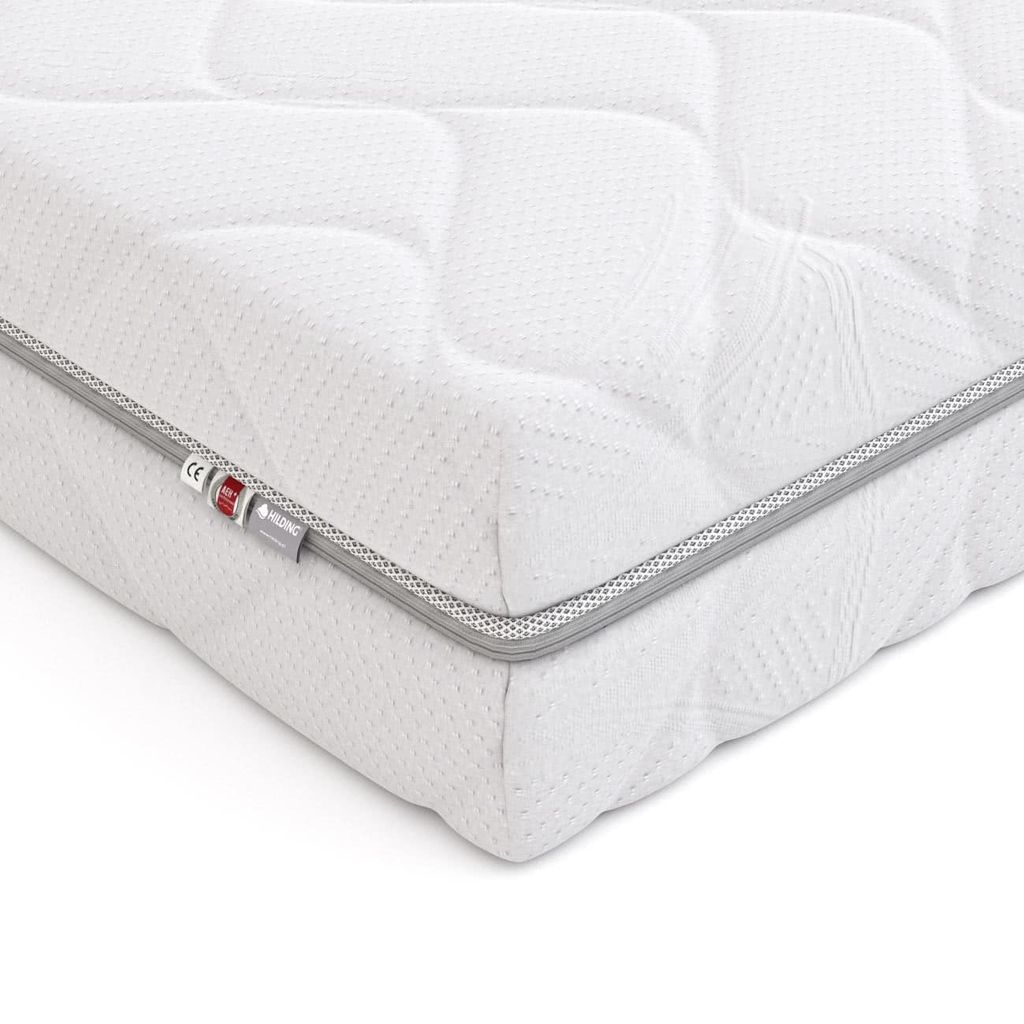 A close-up, angled view of a white mattress with a quilted pattern and a gray trim along the edge. There are small tags attached to the trim.
