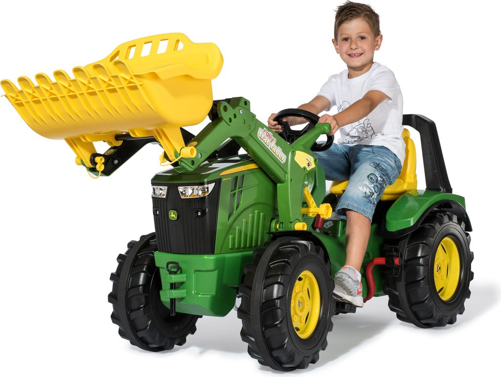A young boy is riding a green and yellow toy tractor with a front loader.