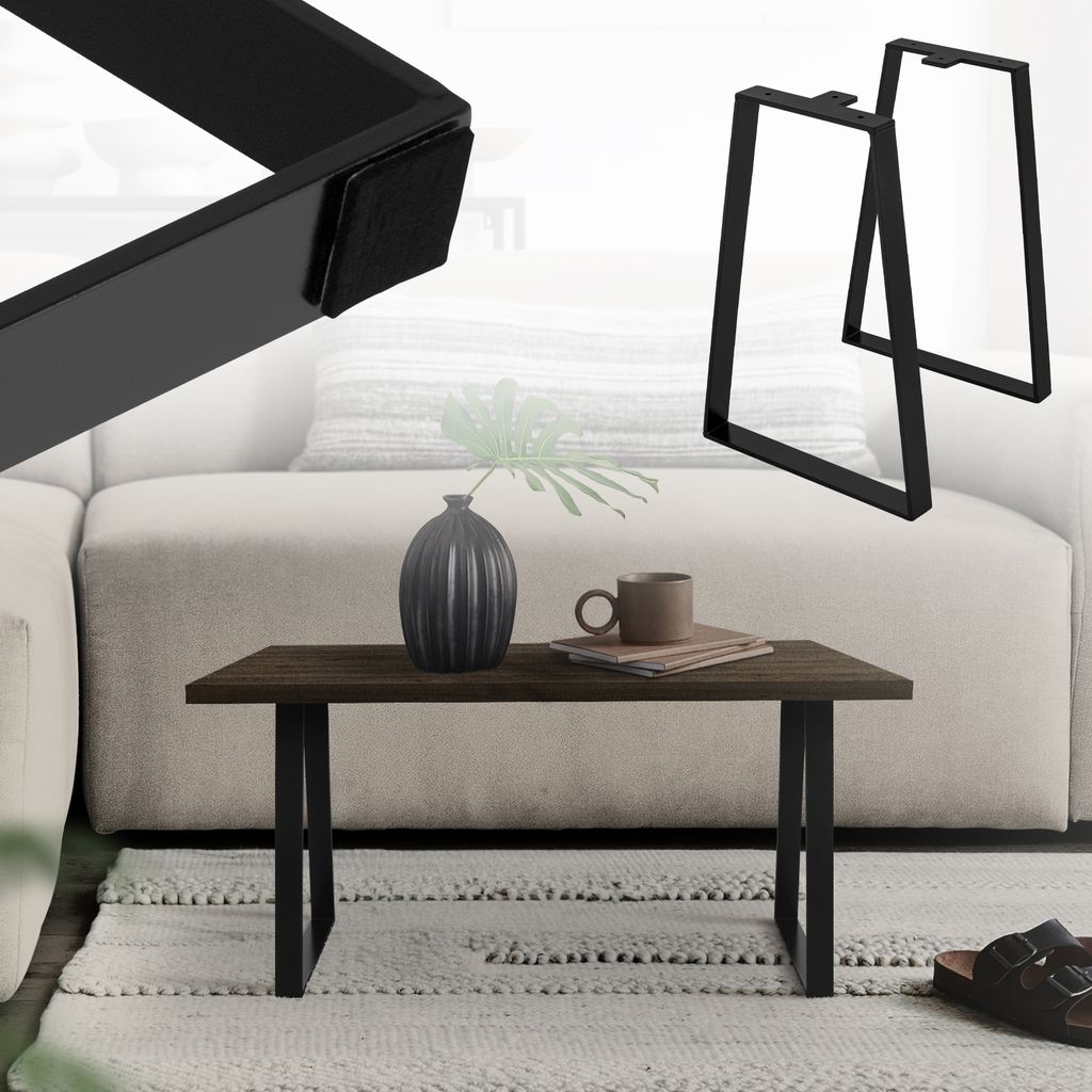 A coffee table with black trapezoidal legs, a dark wood top, a vase, and a mug on a rug in front of a sofa.