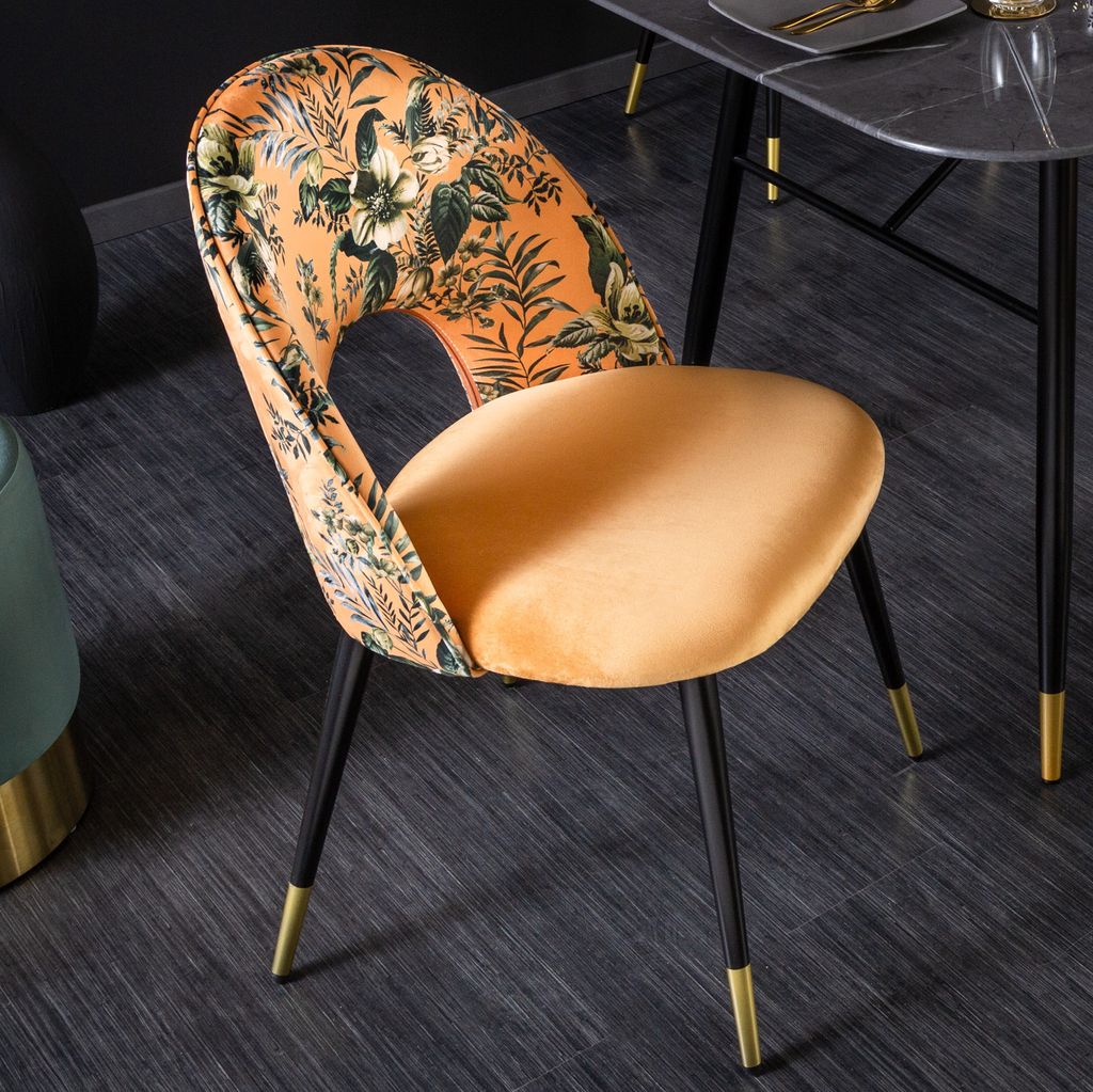 A close-up shot of a designer dining chair with a floral pattern on the backrest and a velvet seat.