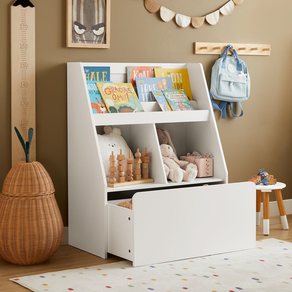 A child's room with a white bookshelf filled with books and toys, a growth chart on the wall, and a woven basket.