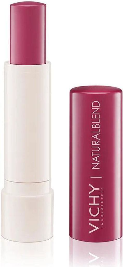A pink tinted lip balm with its cap off, placed next to the cap.