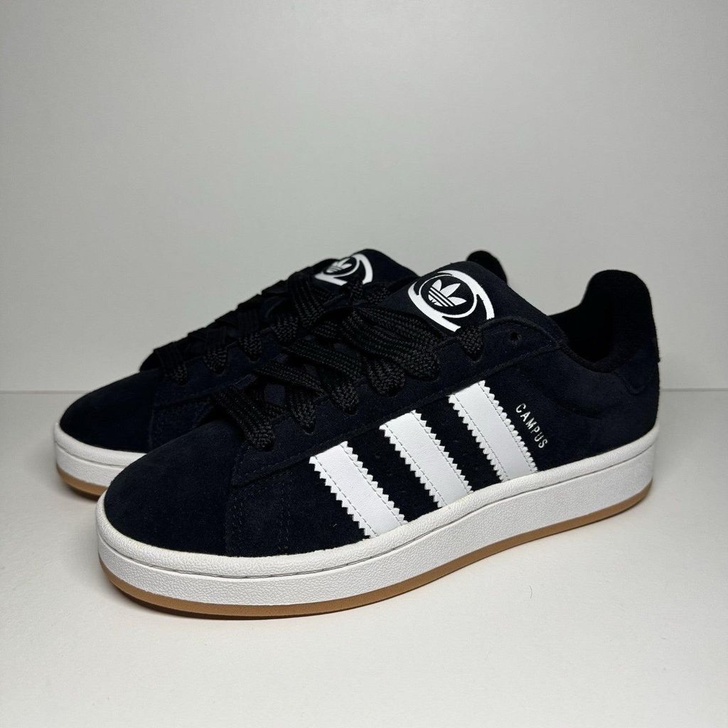 A pair of black Adidas Campus 00S J sneakers with white accents, displayed on a light gray and white background.