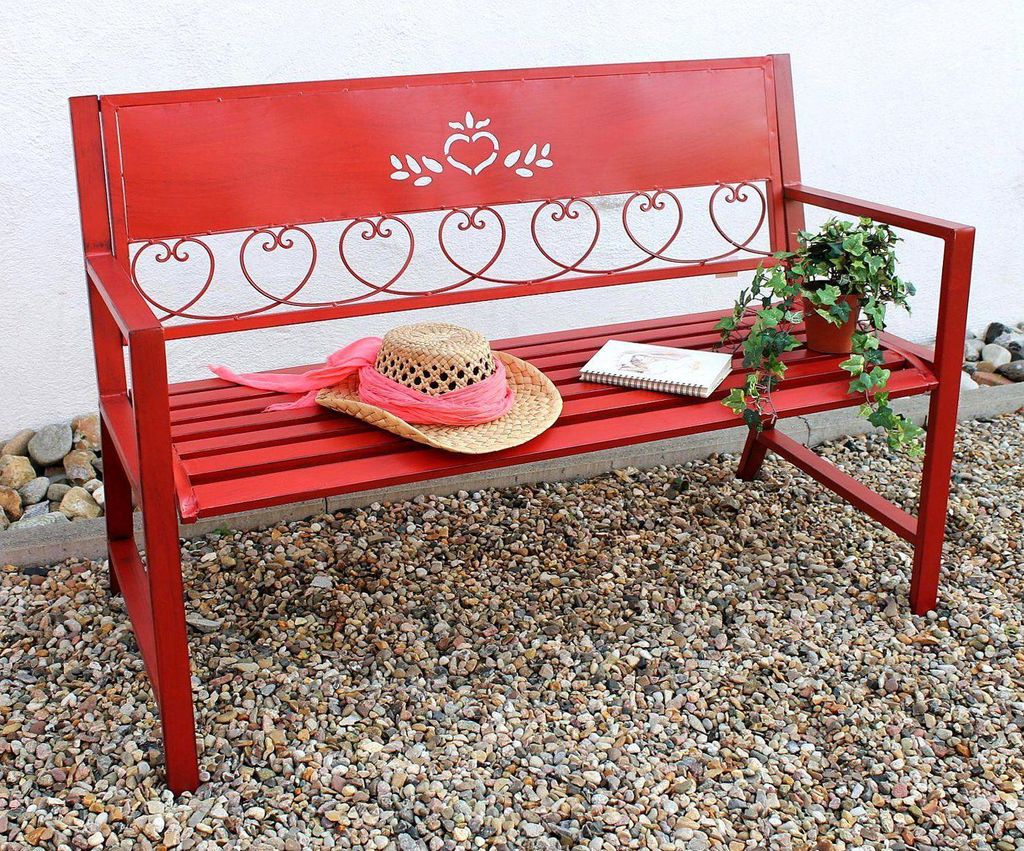 A red metal garden bench with decorative heart cutouts, adorned with a straw hat and a small potted plant.