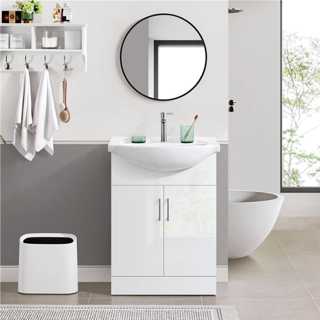 A modern bathroom vanity with a sink and cabinet, a round mirror above, and towels hanging on a shelf.
