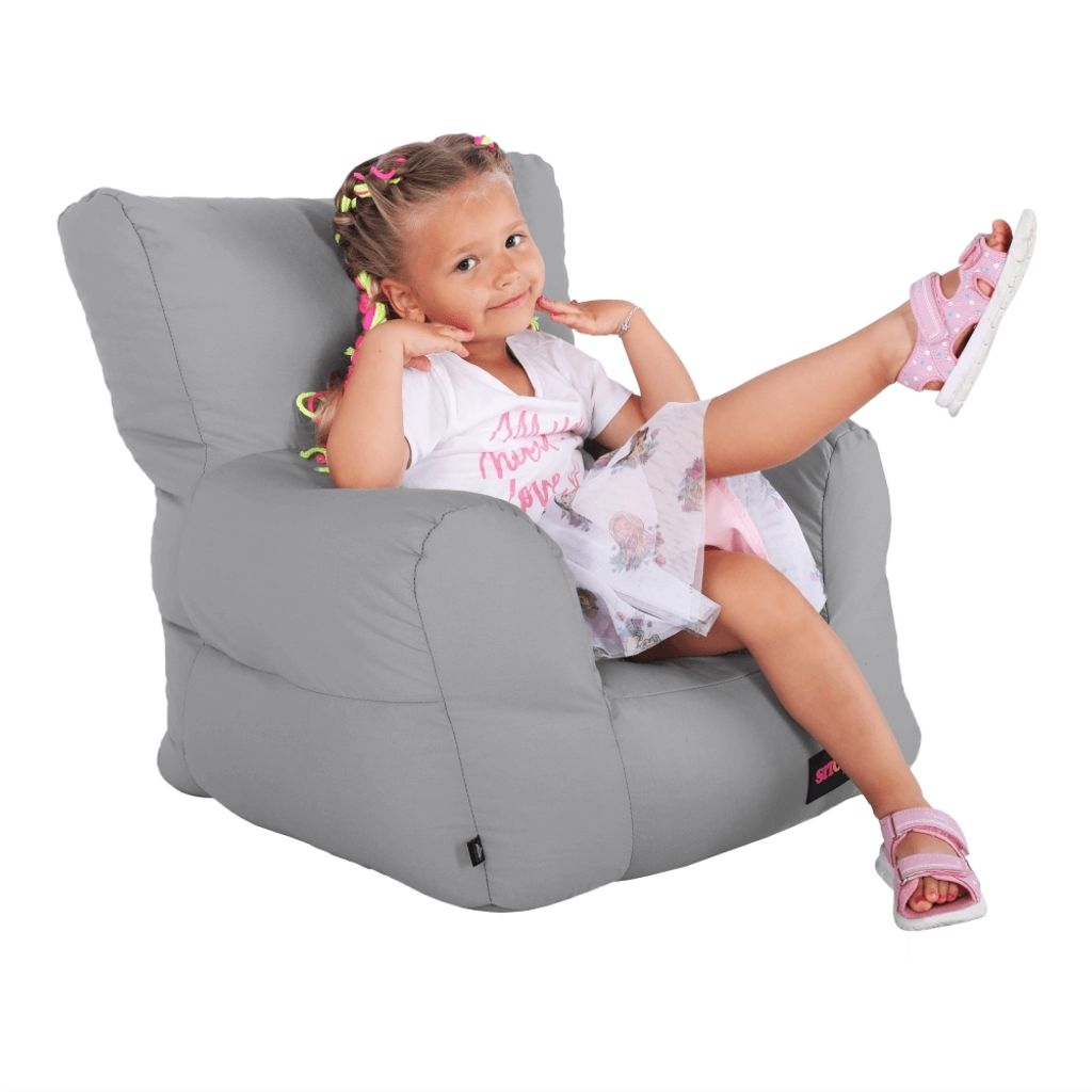 A young girl is sitting in a gray beanbag chair, posing for the camera.