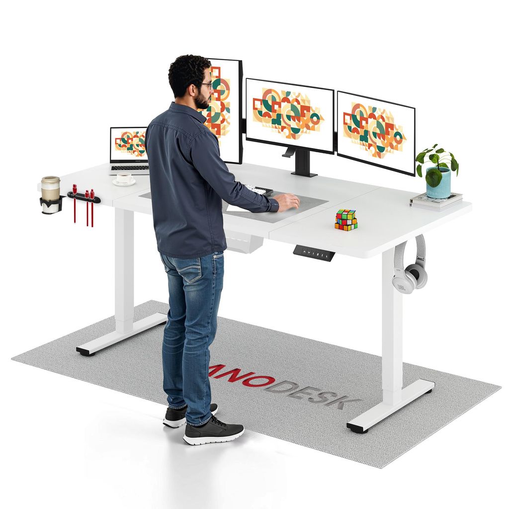 A man is standing at a white standing desk with multiple monitors, a laptop, and office accessories.