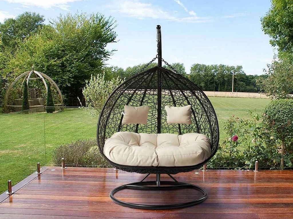 A hanging egg chair with cushions is placed on a wooden deck in a garden setting.
