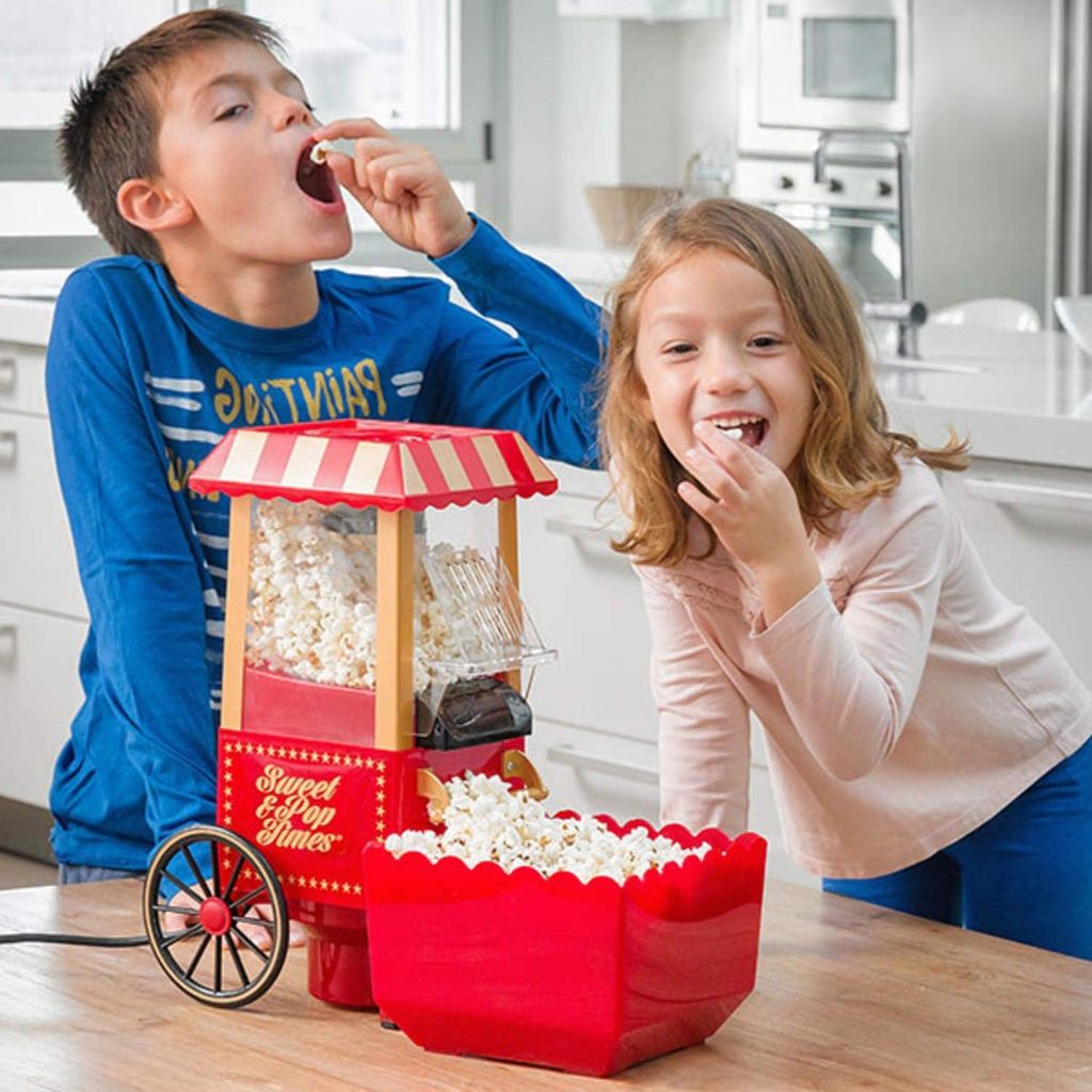 Two children are enjoying popcorn from a popcorn machine in a kitchen.