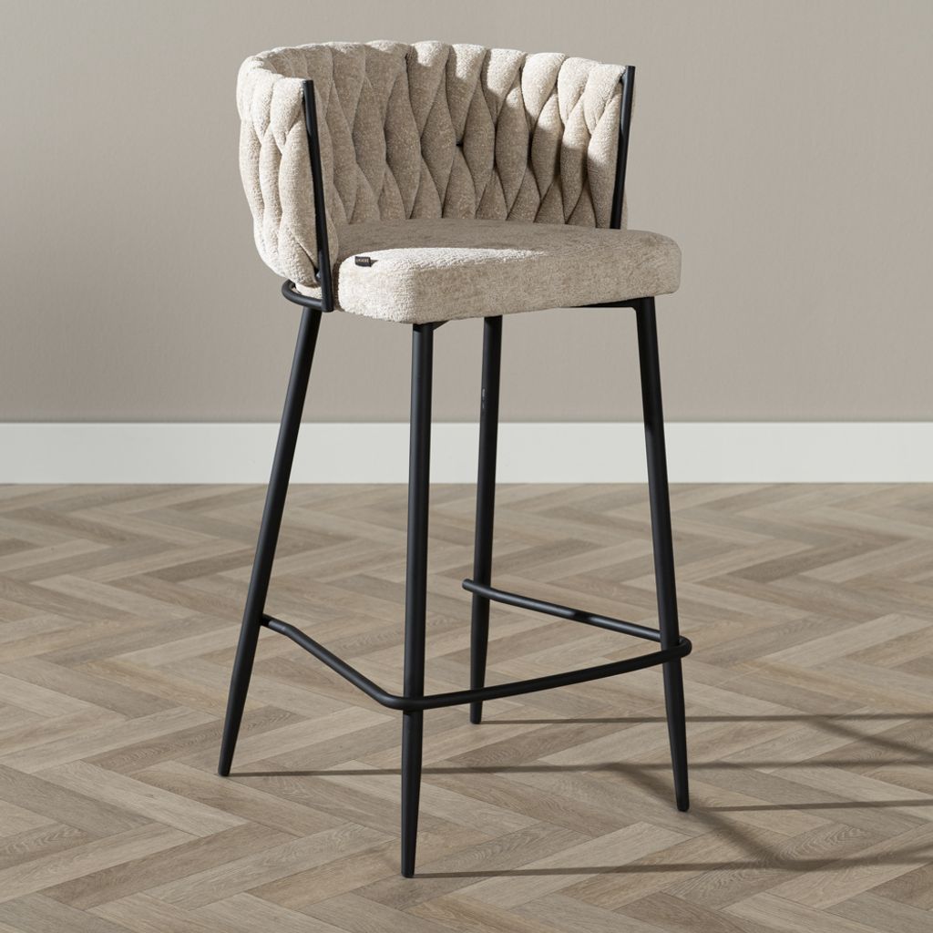 A bar stool is shown in a studio setting against a plain wall and on a wooden floor.