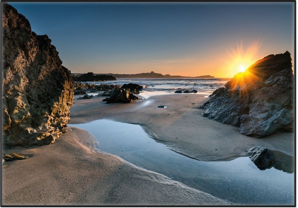 Wallario Wandbild Sonnenuntergang hinter einem Felsen am Strand, Größe: 70,30 x 100,30 cm, Poster mit schwarzem Aluminiumrahmen
