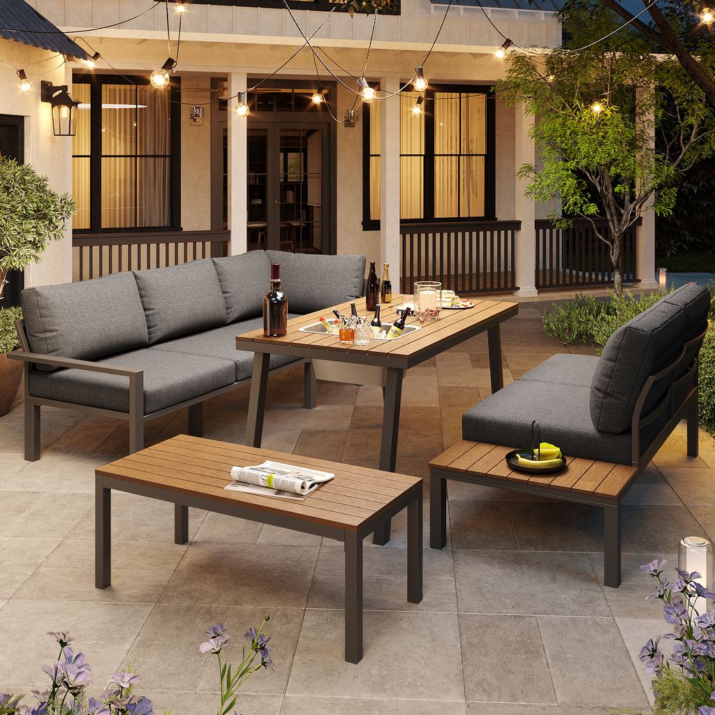 An outdoor patio scene at dusk, featuring a modular outdoor sofa set with a coffee table and a side table. String lights are visible overhead, and plants are in the foreground.