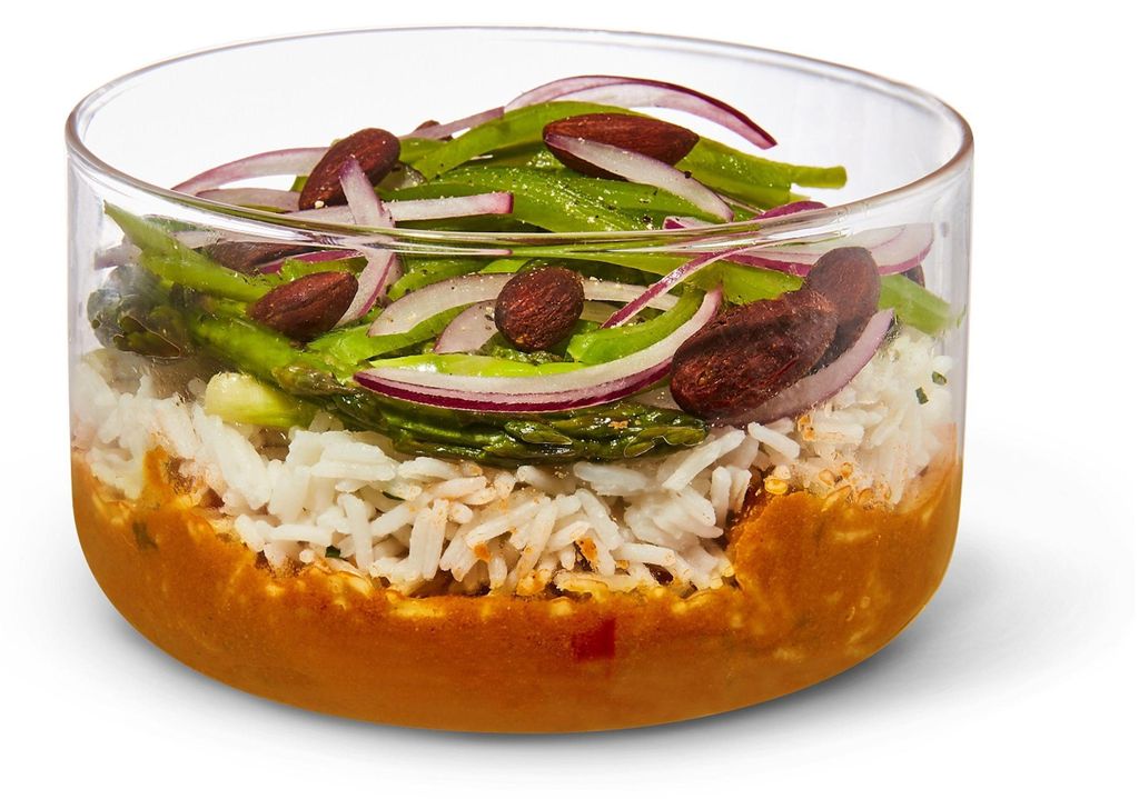 A glass bowl filled with rice, vegetables, and almonds.