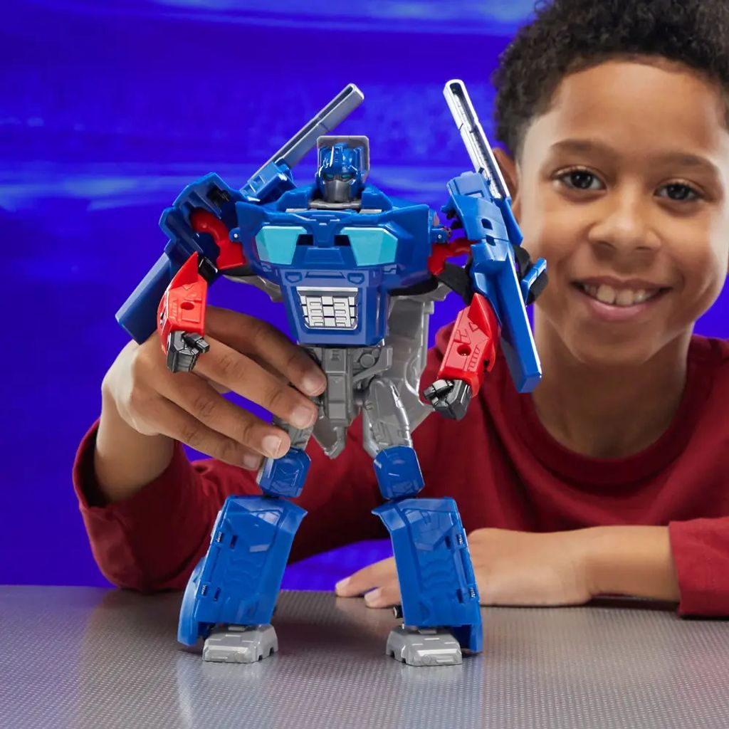 A young boy is smiling and holding a blue and gray robot toy.