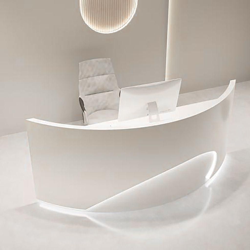 A modern, white reception desk with a curved design and integrated lighting, along with a computer monitor and a chair.