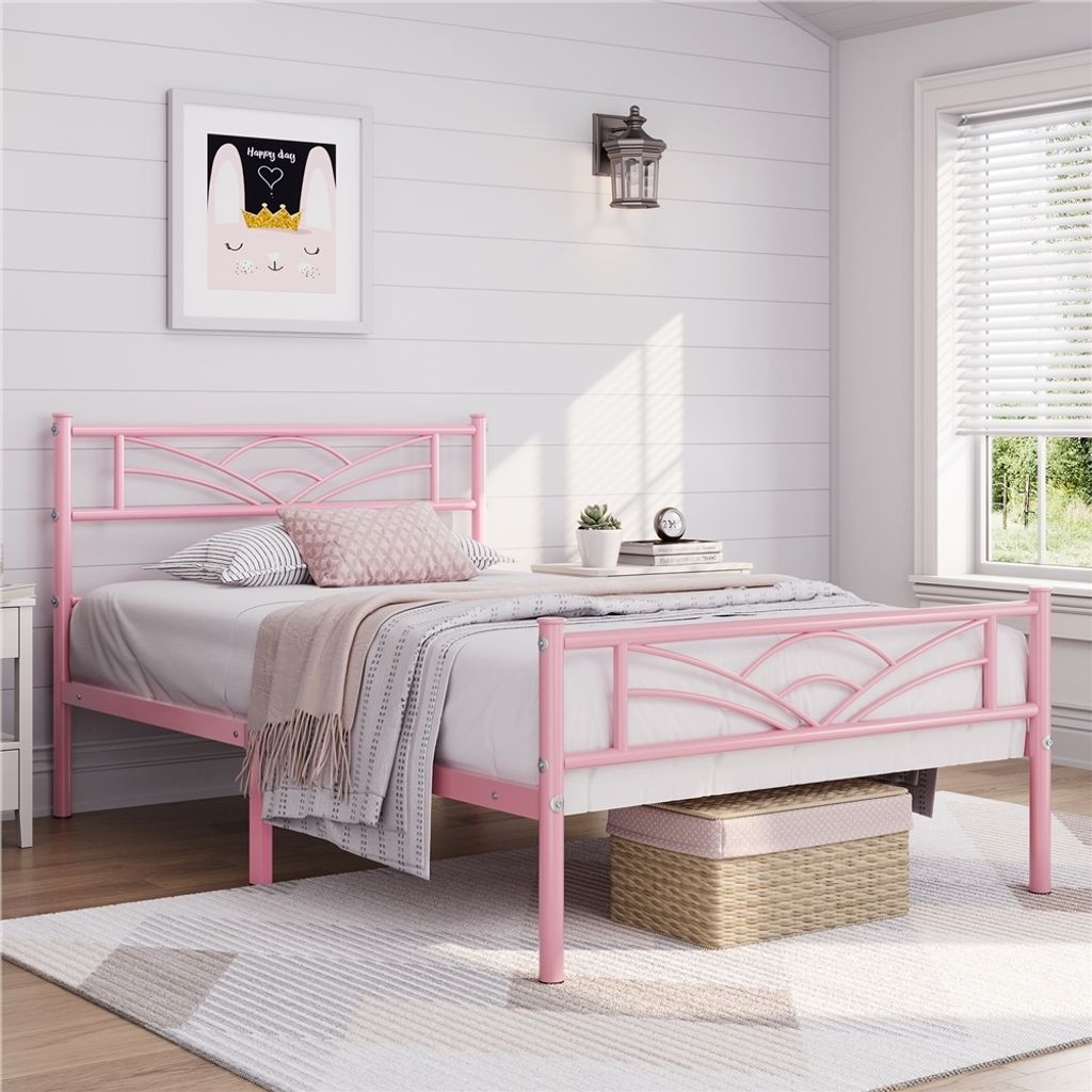 A pink metal bed frame with a cloud pattern headboard, set up in a bedroom with a framed picture on the wall and a window with blinds.