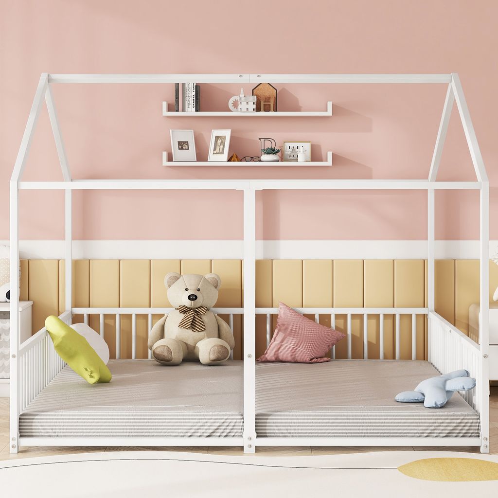 A white metal house-shaped bed frame with two mattresses, a teddy bear, and pillows.