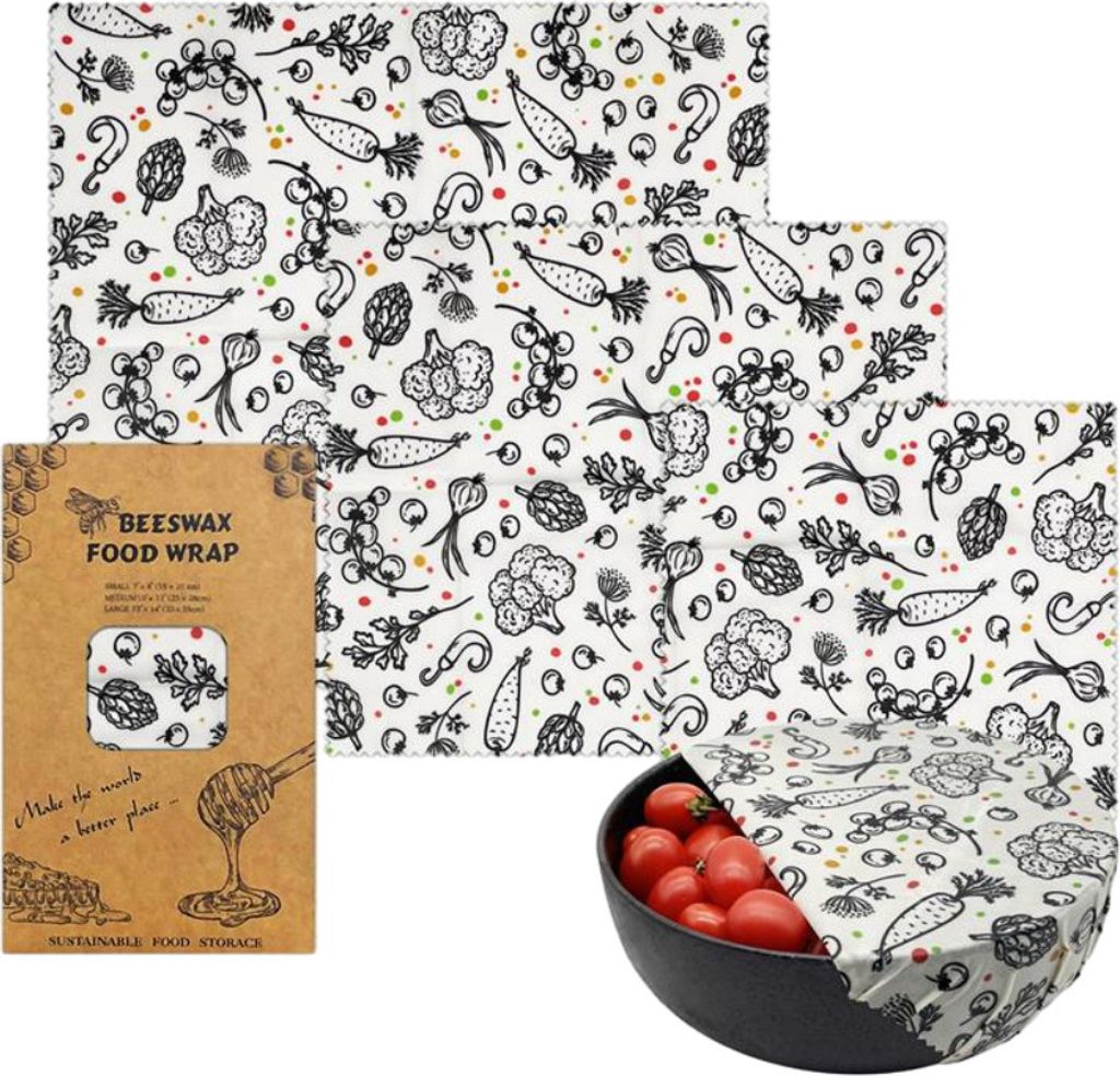 A set of beeswax food wraps with a vegetable pattern, displayed with packaging and a bowl of tomatoes.