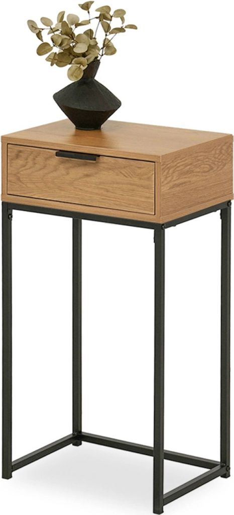 A narrow console table with a wooden top and a single drawer, supported by black metal legs. A black vase with dried foliage sits on top.