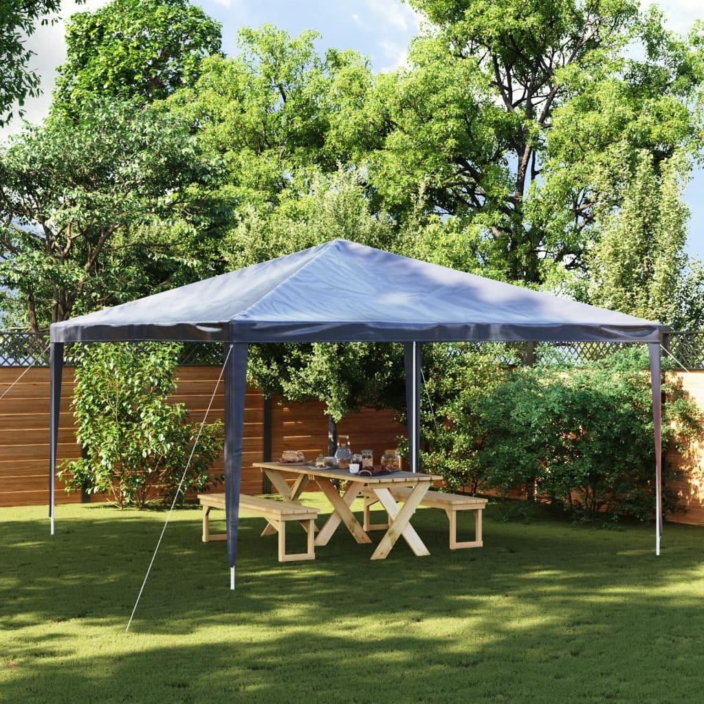 A party tent set up in a backyard with a picnic table and benches.
