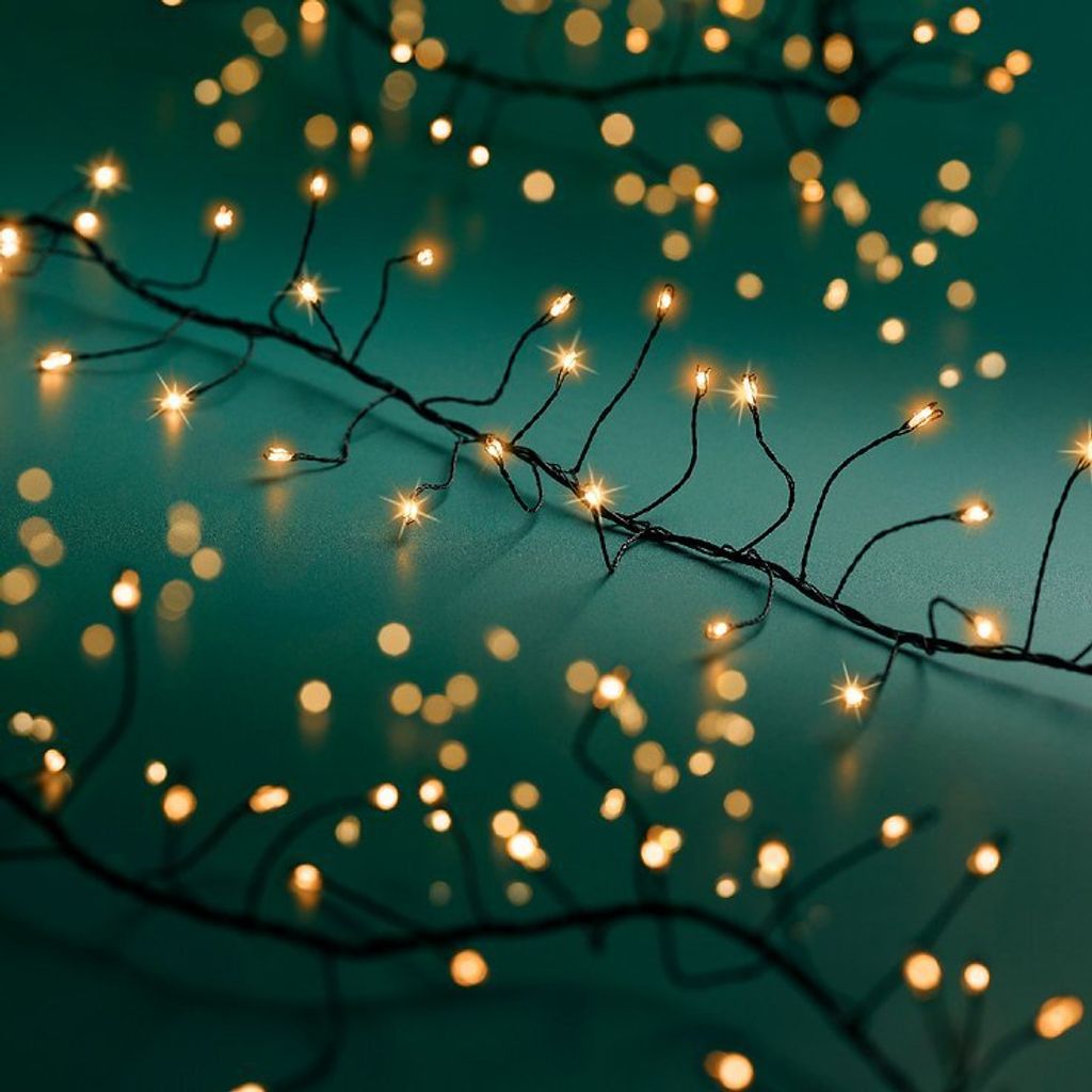 A close-up shot of a string of warm white LED lights on a black wire against a teal background.