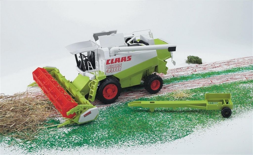 A toy combine harvester is shown on a diorama of a field with grass and dirt.