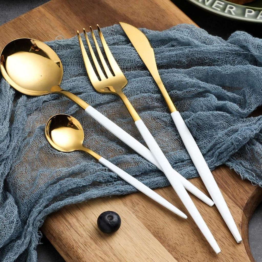 A set of gold and white cutlery laid out on a blue cloth on a wooden board.