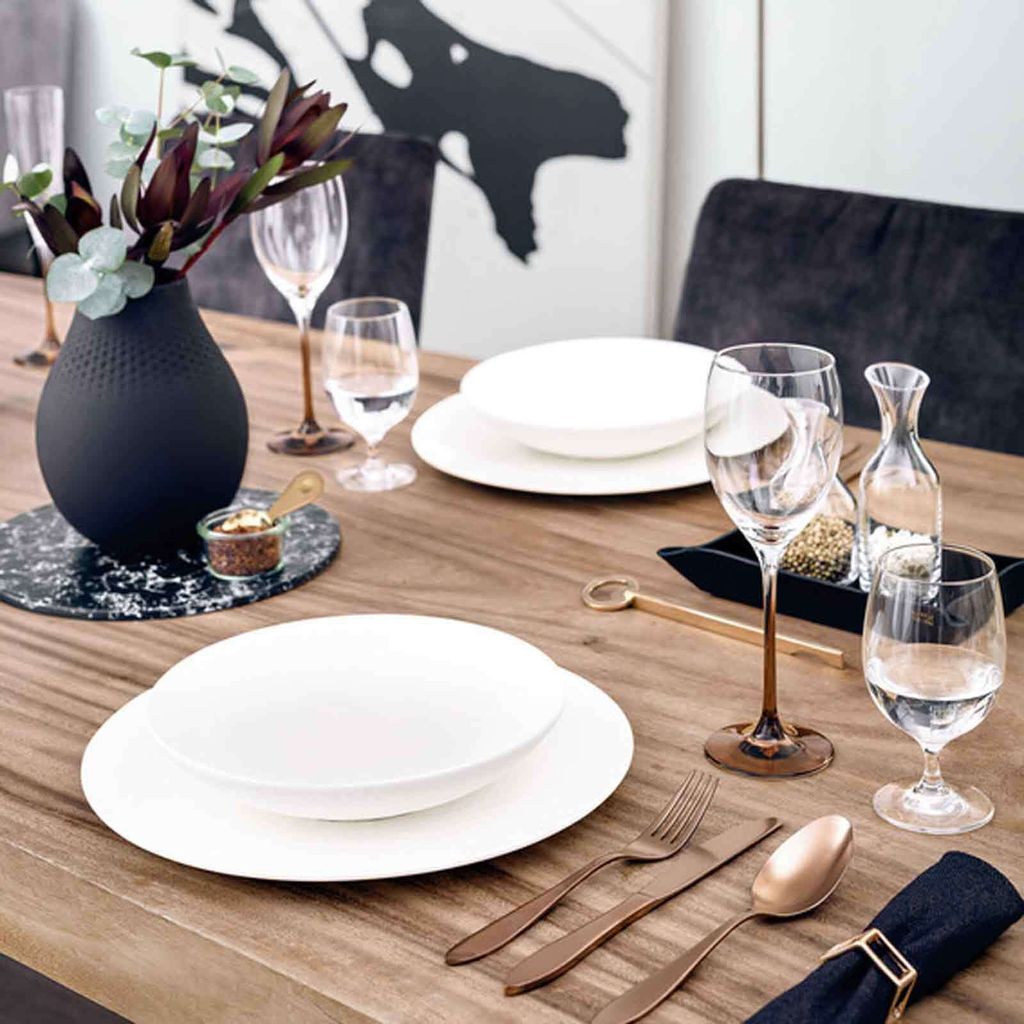 A table setting with plates, glasses, cutlery, and a vase with flowers.