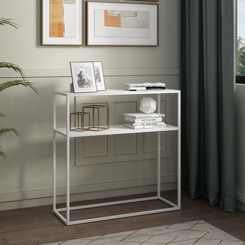 A white console table with two shelves, decorated with picture frames, books, and decorative objects, placed in a room with a plant and curtains.