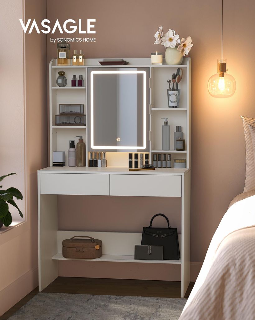 A white vanity table with a lighted mirror and shelves filled with makeup and accessories, placed in a bedroom setting next to a bed.