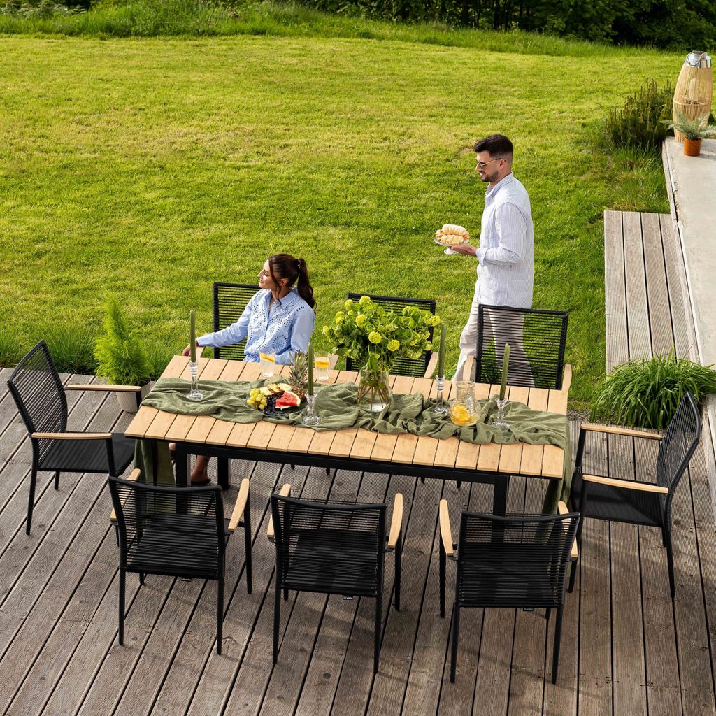 A couple is enjoying a meal outdoors at a table set on a wooden deck, with a lush green lawn in the background.