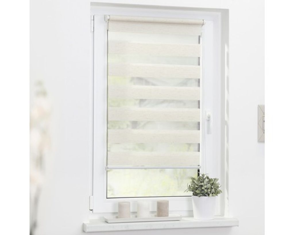 A roller blind is installed on a window, with a small potted plant and two candles on the windowsill below.