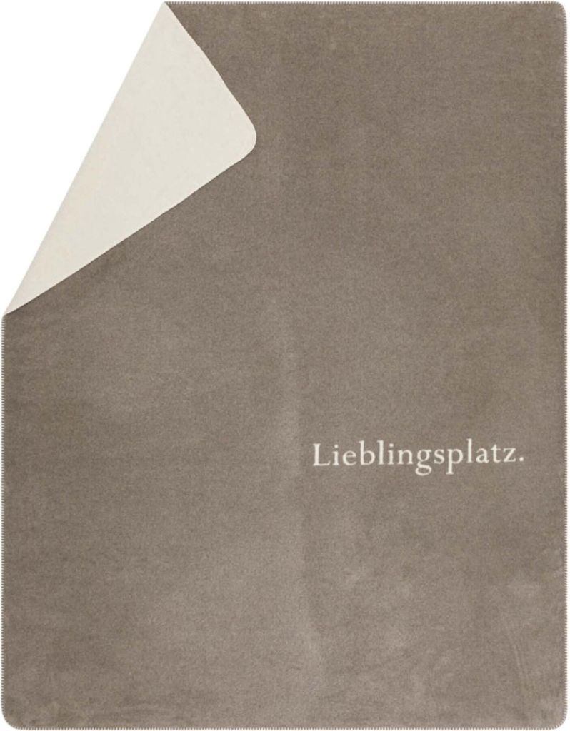 A folded blanket with a corner lifted, revealing a different color underneath. Text is present on the blanket.