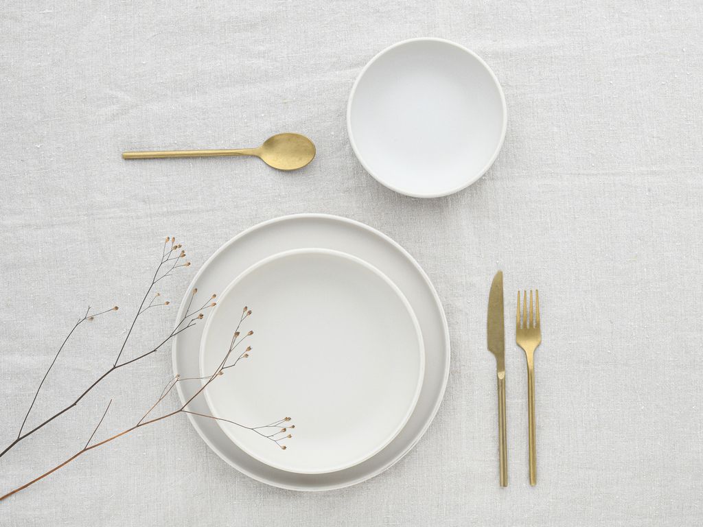 A minimalist table setting with white plates and gold cutlery.