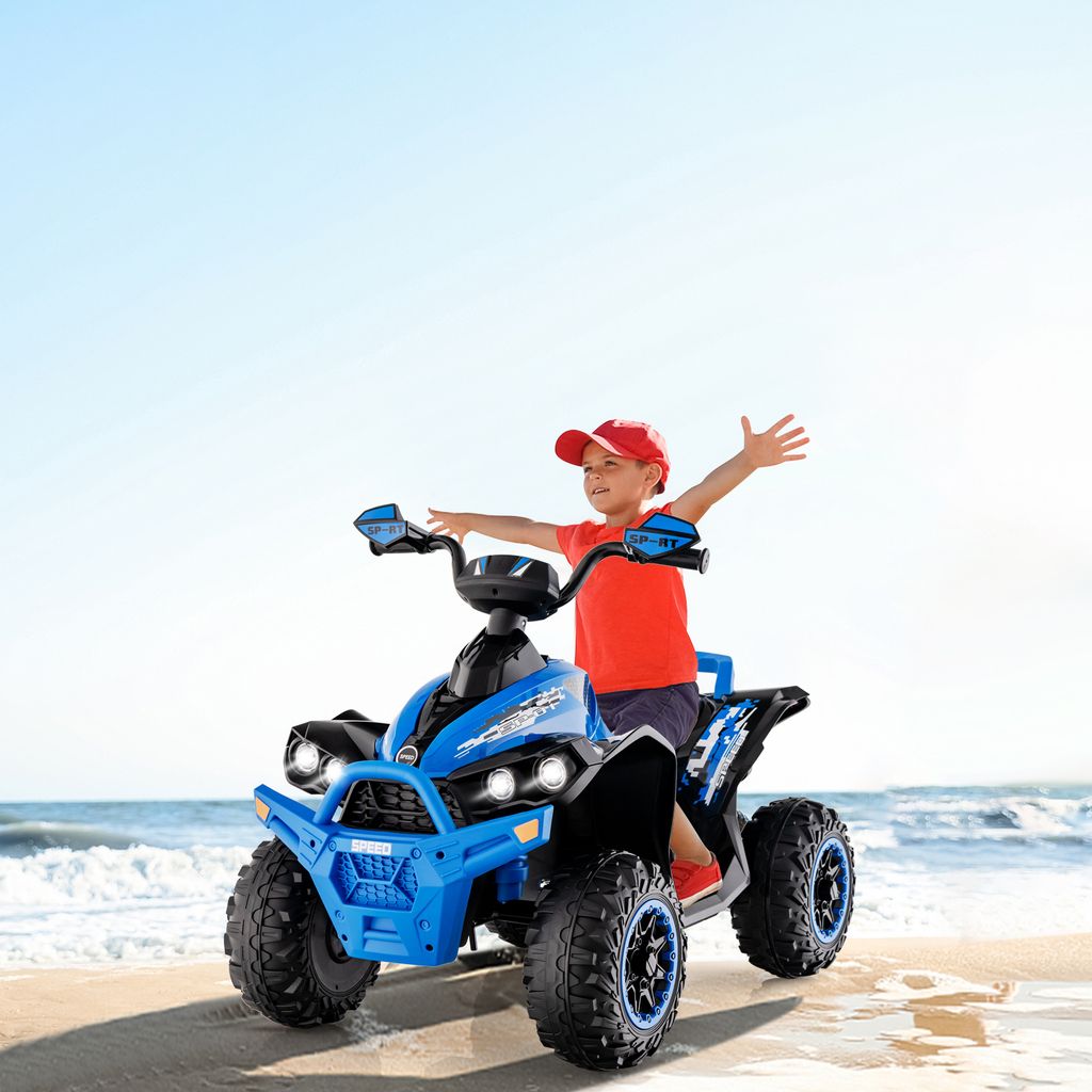 A young boy rides a blue electric quad bike on a beach with the ocean in the background.