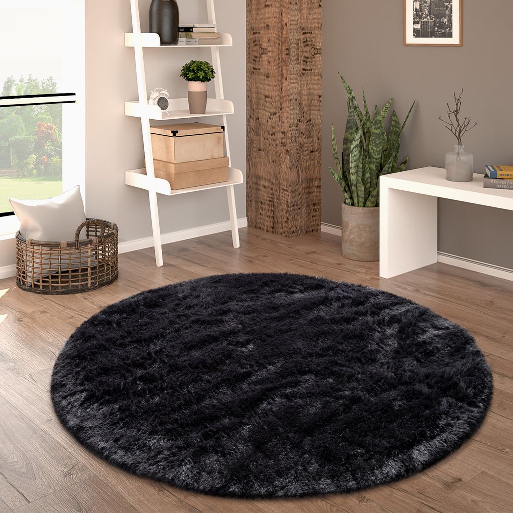 A round black shaggy rug is placed on a wooden floor in a living room setting, next to a ladder shelf and a plant.
