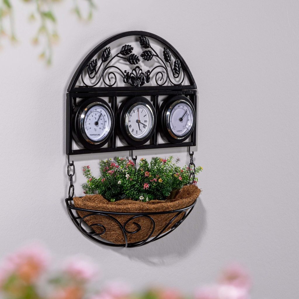 A black metal wall-mounted planter with three thermometers and a basket filled with green plants and pink flowers.