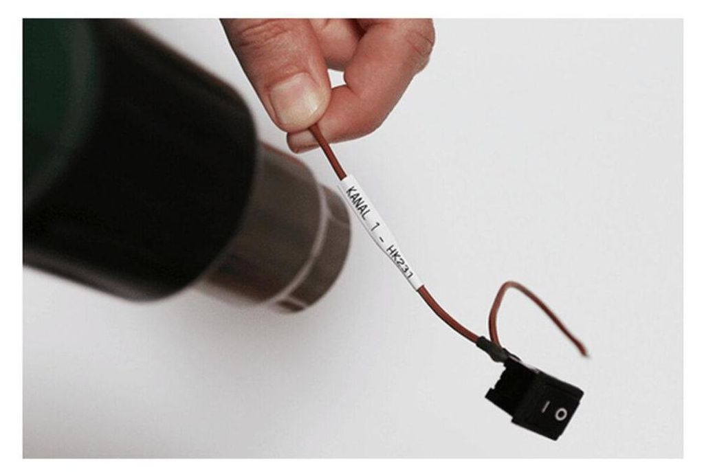 A hand holds a wire with a label and a switch attached to it, with a dark object in the background.