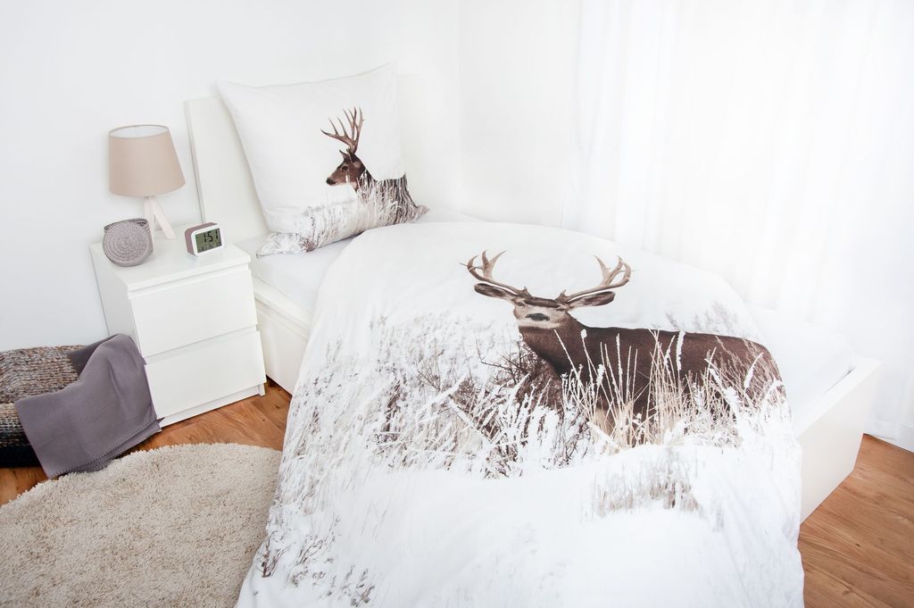 A bedroom scene with a bed dressed in deer-themed bedding.