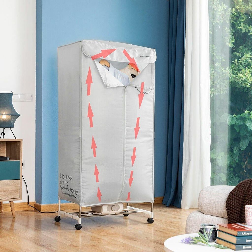 A portable electric clothes dryer is shown in a room with a blue wall, a window with curtains, and furniture. Arrows indicate airflow within the dryer.