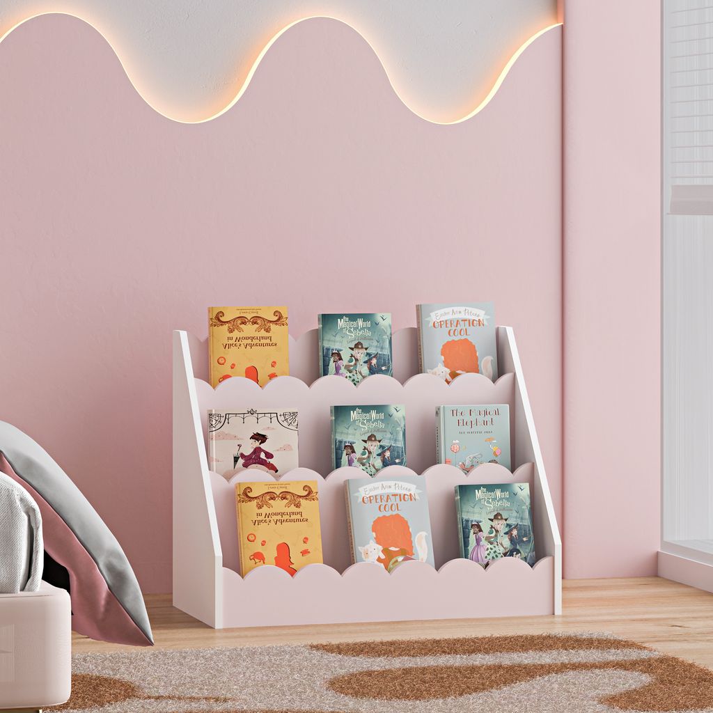 A child's bedroom with a pink wall, a white scalloped bookshelf filled with children's books, and a glimpse of a bed and rug.