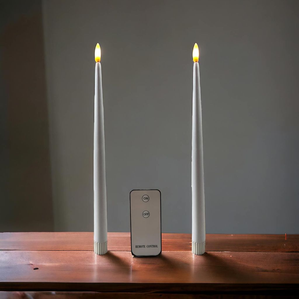 Two white LED taper candles with a remote control placed between them on a wooden surface.