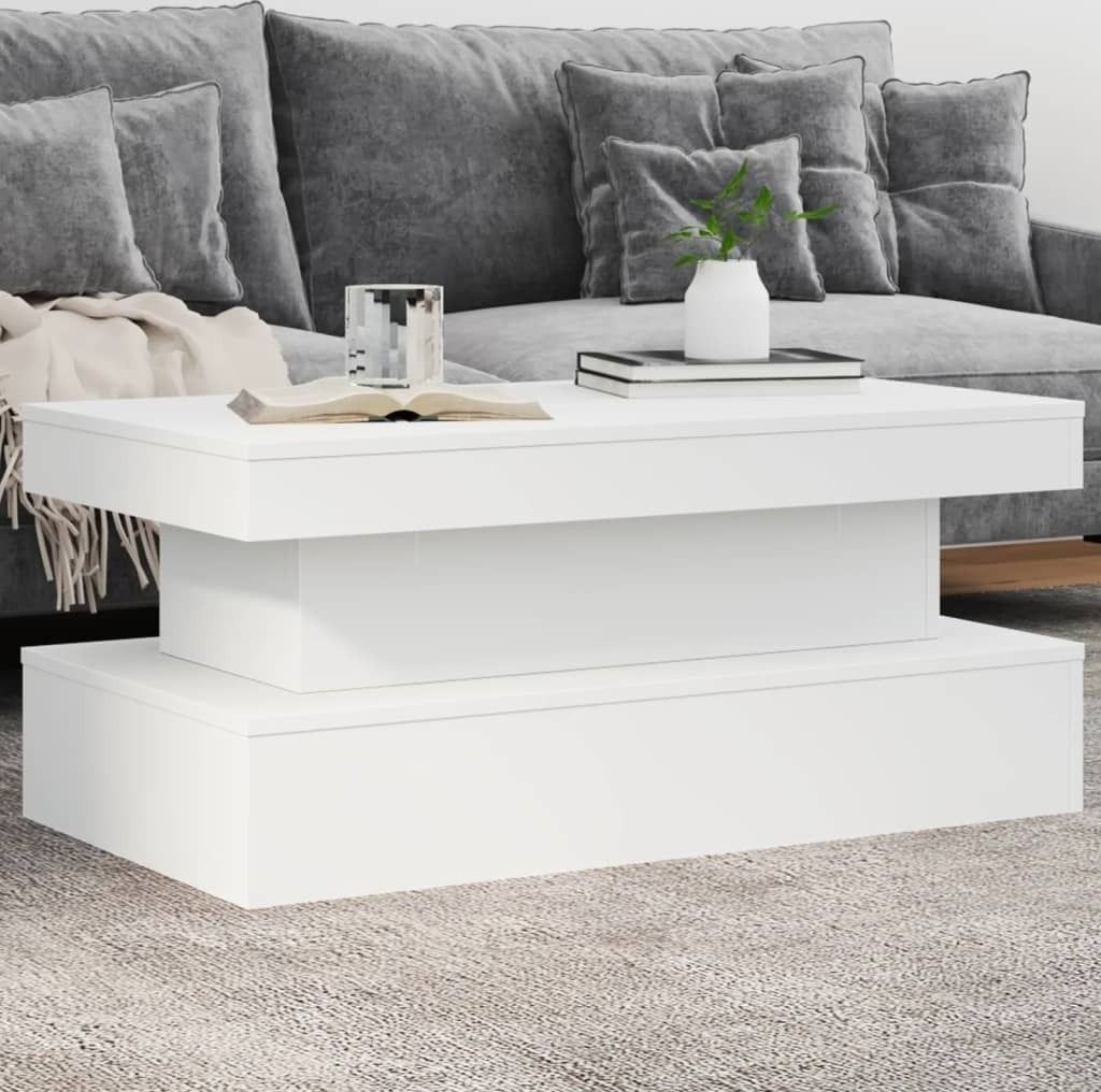 A white coffee table with a book and a vase on it, placed in front of a gray sofa.