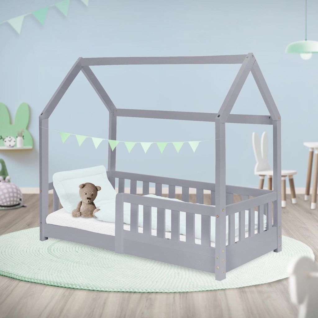 A child's bedroom with a grey house-shaped bed, a teddy bear on the mattress, and decorative bunting.