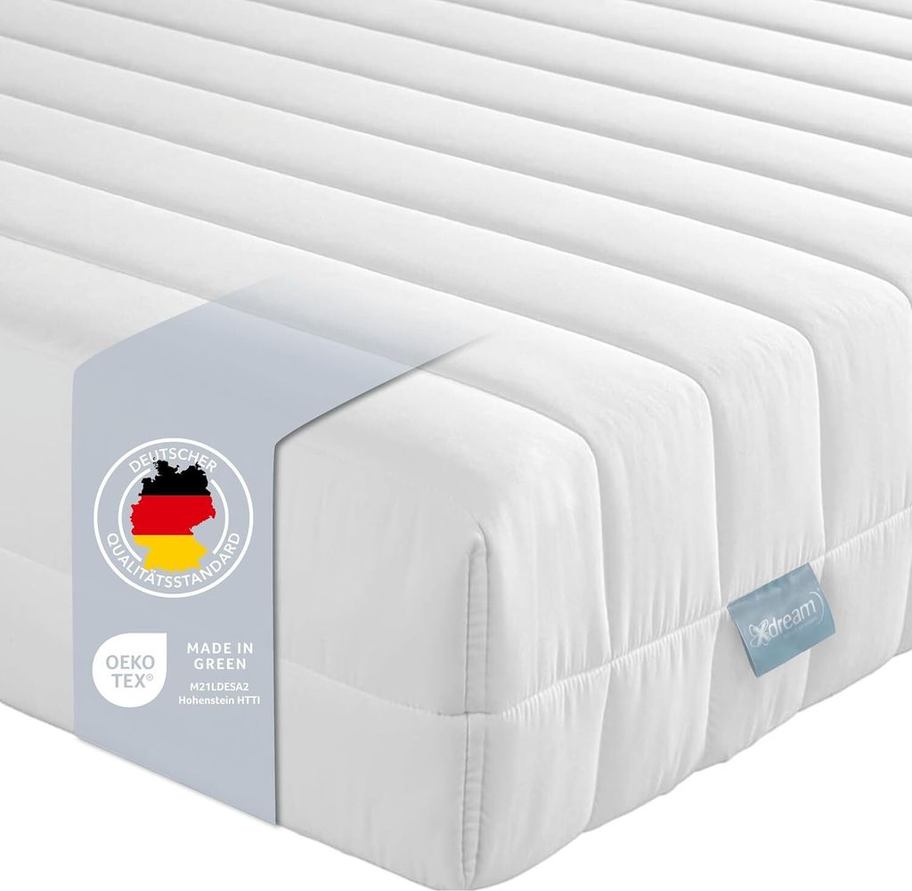 A close-up, angled view of a white mattress with a blue label and a grey band with German flag and certifications.